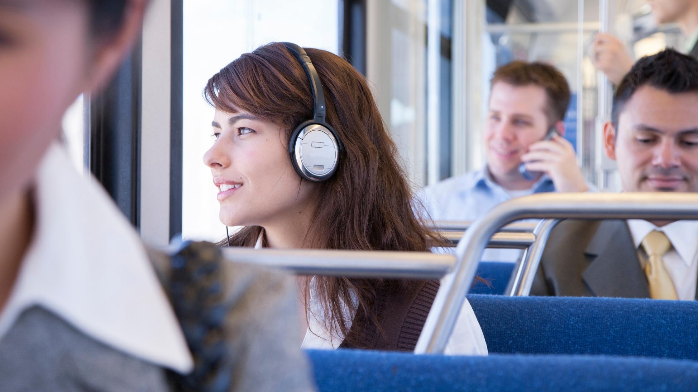 young person wearing headphones on a bus with other commuters