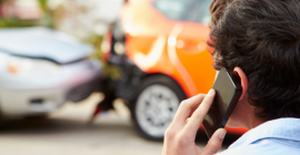 The back of a man's head while he talks on a cell phone. An orange car is out of focus in the background. 