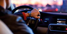 The shoulder and hand of a person driving a car at sunset. 